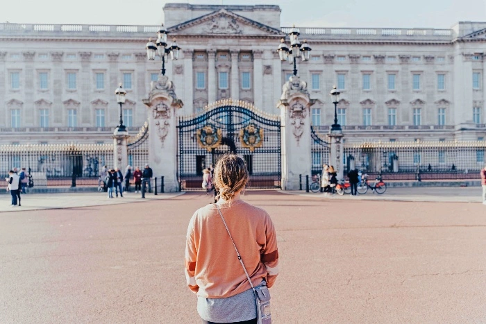 A woman wearing a pink sweater standing in front of Buckingham Palace in London