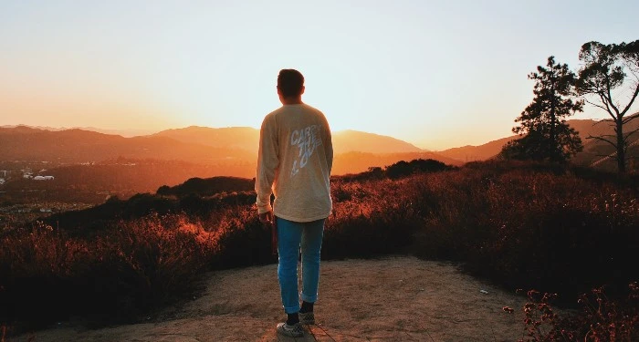 A man in a tshirt and jeans watches a sunset