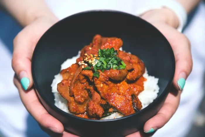 A woman with green fingernails holding a bowl of red bulgogi on white rice
