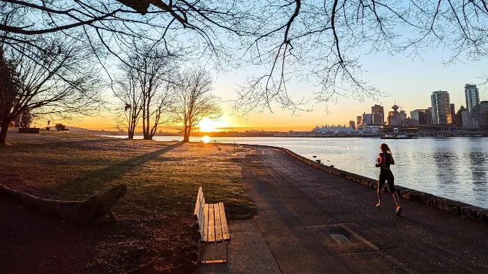 A woman jogging at sunrise in Stanley Park overlooking Vancouver Downtown