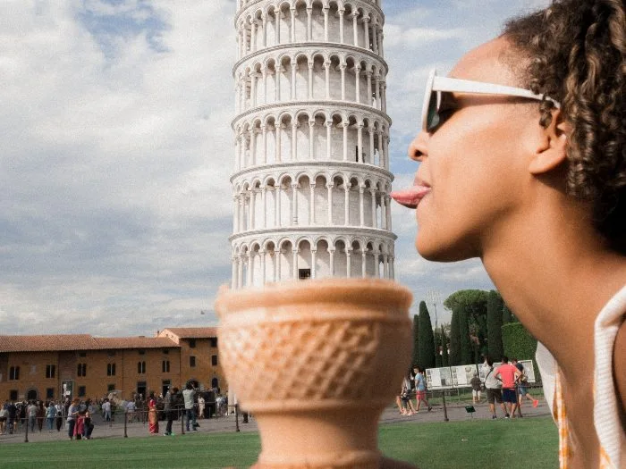 A depth perception photography trick creates the illusion that the Leaning Tower of Pisa is a ice cream in a cone being licked by a woman