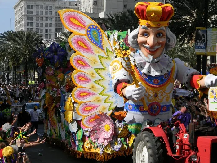 A colorful float featuring a court jester is pulled by a red tractor in a Mardi Gras parade in New Orleans