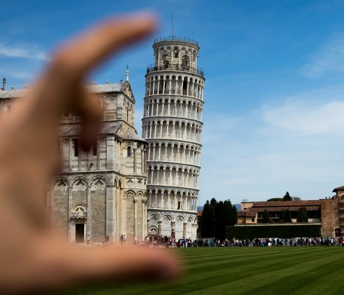 An optical illusion making it appear as if a hand is about to squish the Leaning Tower of Pisa