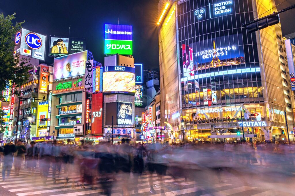 Neon-lit Shibuya Crossing at night, evoking the bustling cityscapes in 'Tokyo Ghoul.'