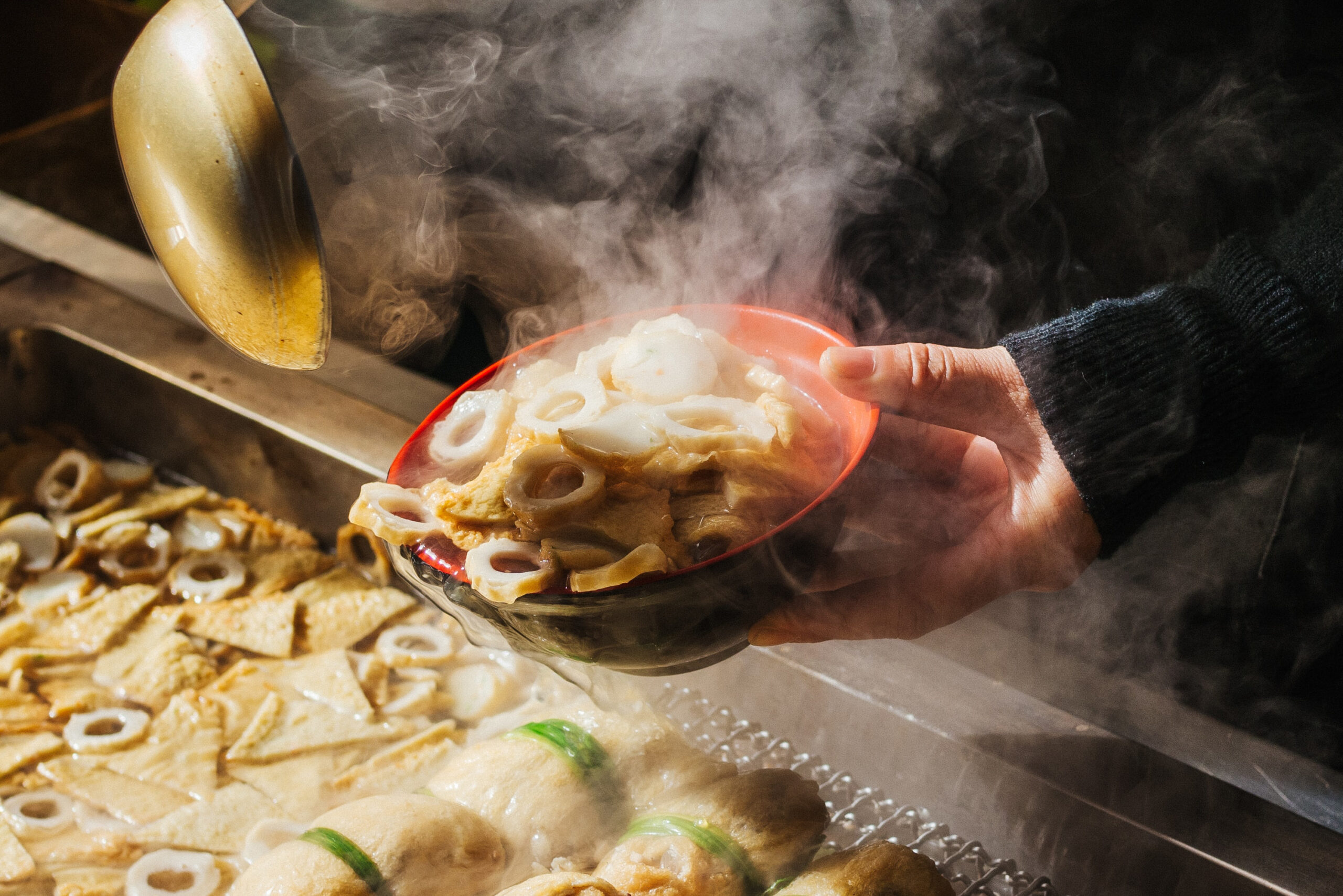 Hand holding a steaming bowl of traditional Korean udon, highlighting the warm, street food culture in Korea.