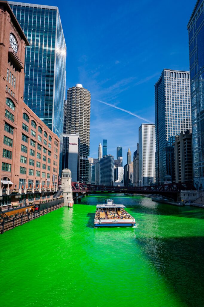Chicago River dyed green with a tour boat, surrounded by iconic city architecture, during St. Patrick's Day celebrations