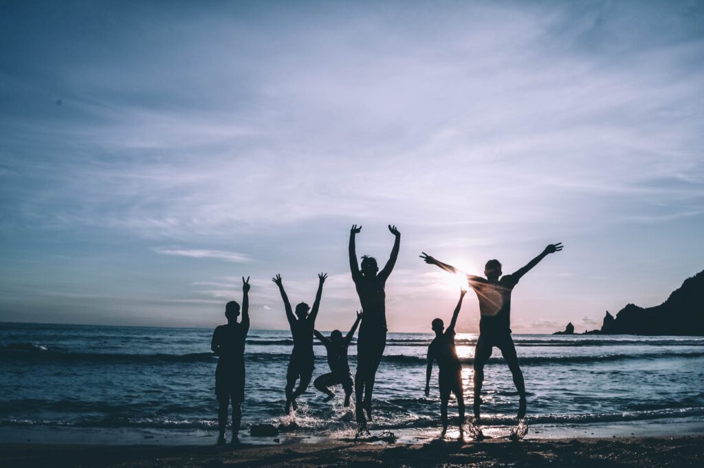 An image of a young group of college students excited as they just arrived to the beach. It is a group of 6 of them jumping with joy on the shore.