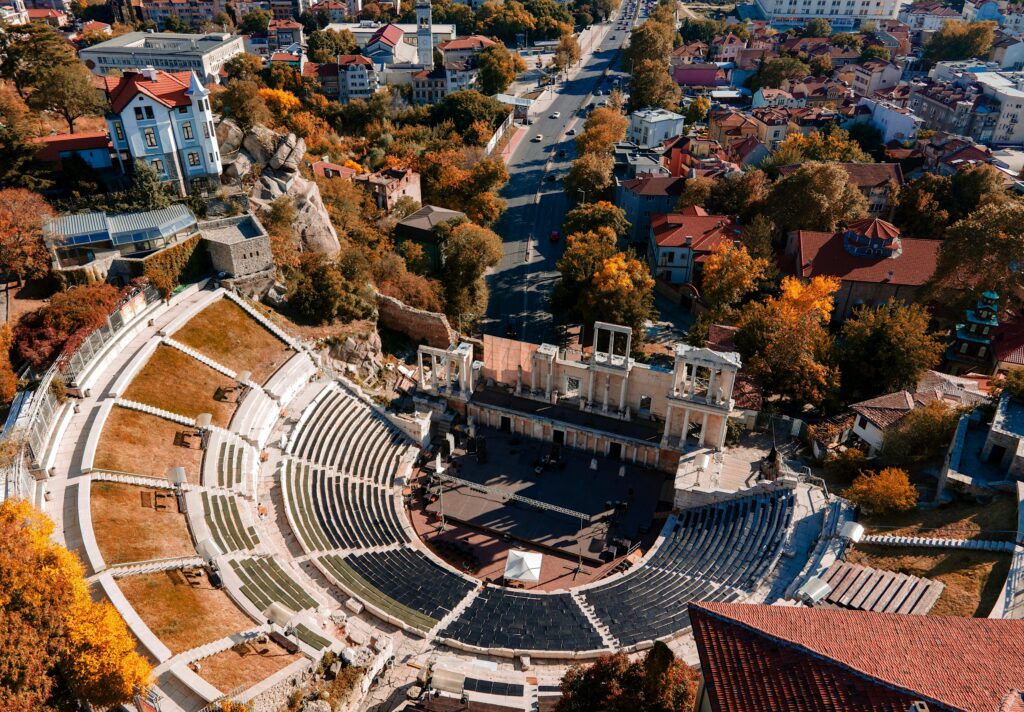 Ancient amphitheater nestled in a vibrant cityscape with autumn-colored trees, perfect for history-loving students on a study abroad semester looking to immerse in historical sites.