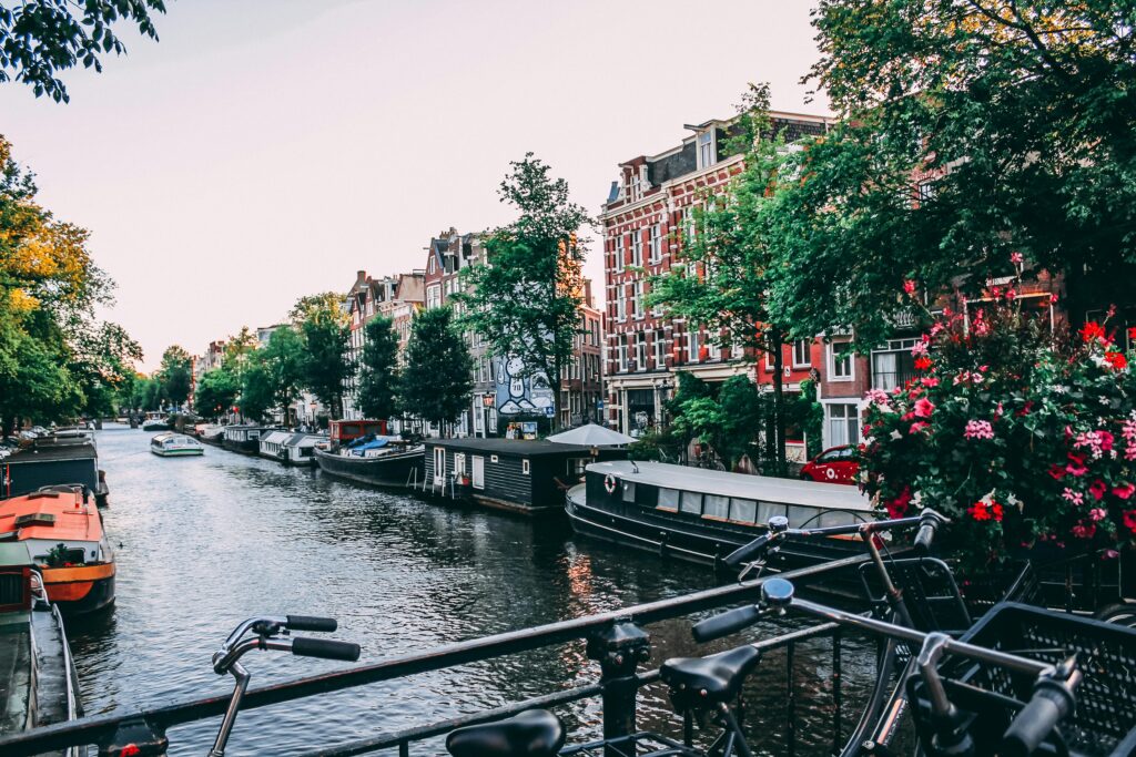 Picturesque Amsterdam canal with eco-friendly bicycles and flower-decked houseboats, popular with environmentally-conscious student travelers