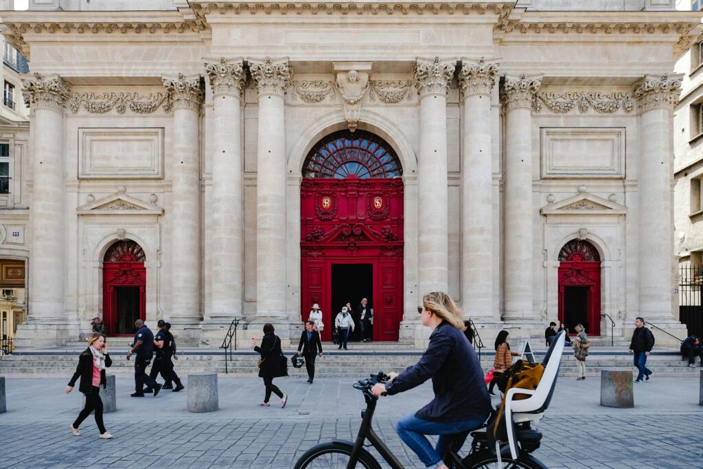 Cyclist passing by an iconic red-door landmark building in Paris, an architectural gem that appeals to student explorers interested in sustainable urban design.