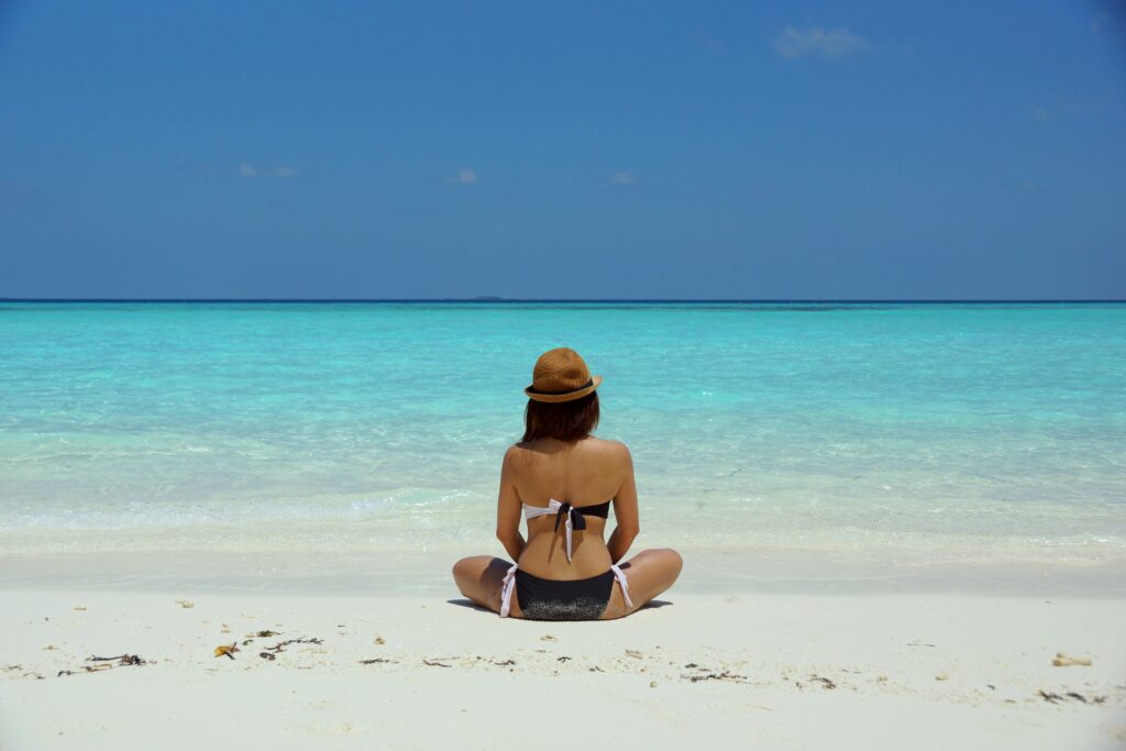 Woman sitting peacefully on a serene South Pacific beach contemplating the horizon, perfect for affordable Mother's Day getaways for students.