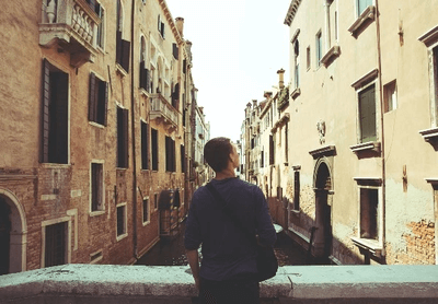 Person standing on a bridge overlooking a narrow canal lined with historic buildings, evoking travel and exploration in a European city.