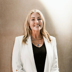 Portrait of a smiling woman wearing a white blazer and black top, presenting a professional and approachable appearance.