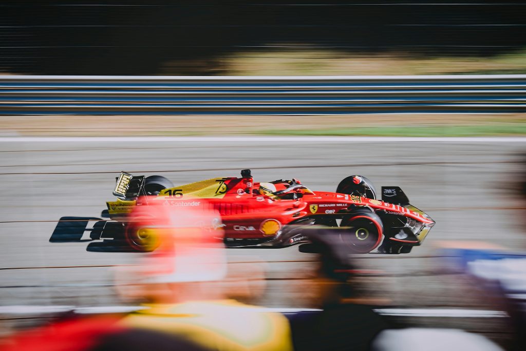 Ferrari Formula 1 race car speeding on a track during a Grand Prix event, with motion blur and spectators in the foreground — high-speed motorsport action captured live.