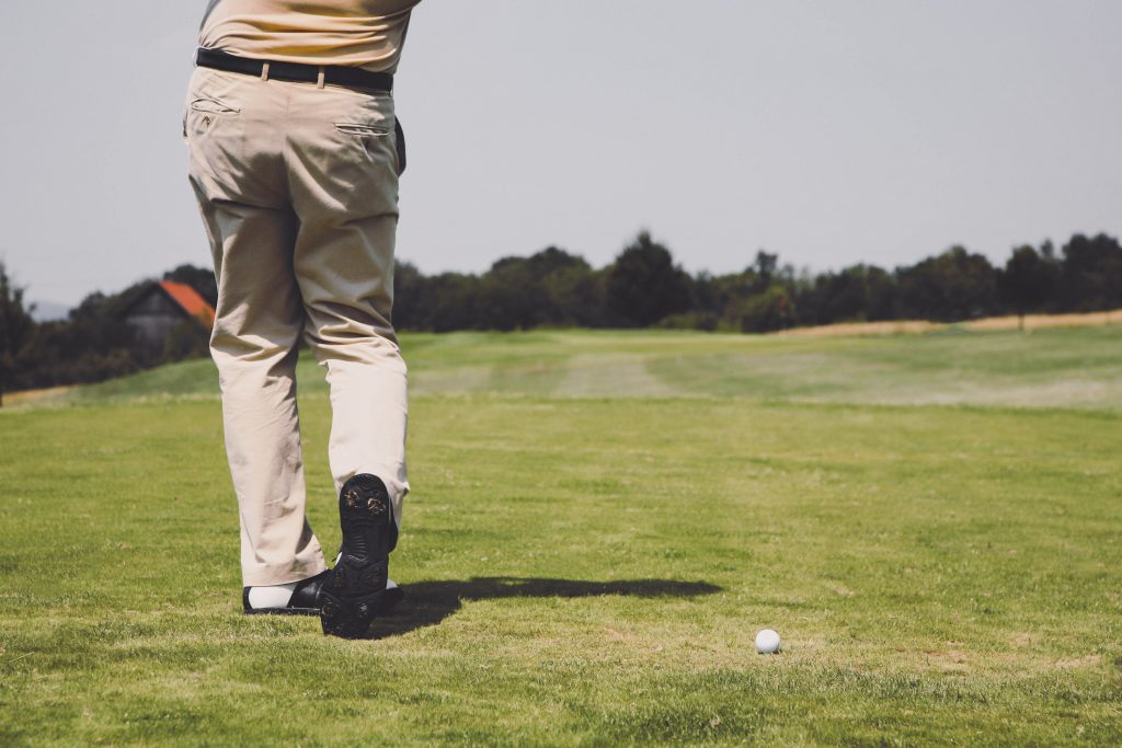 Golfer mid-swing on a sunny fairway, aiming at the green with golf ball in play — scenic golf course in Portugal, ideal for sports travel or outdoor recreation.