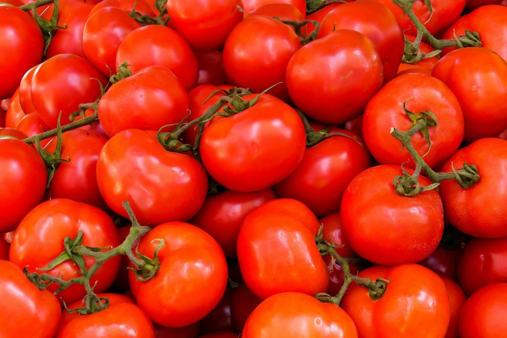 A pile of fresh red tomatoes with green stems, closely packed together, showcasing their ripe and glossy skin.
