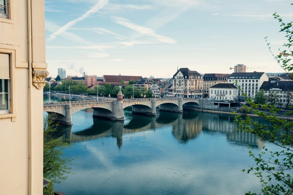 Scenic view of Basel’s Middle Bridge (Mittlere Brücke) spanning the calm Rhine River, surrounded by historic buildings and city reflections on the water.