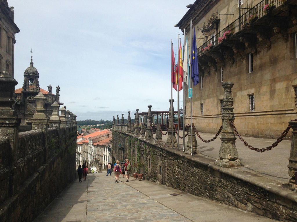 Historic stone pathway leading downhill in Santiago de Compostela, Spain, with flags and centuries-old buildings lining the street near the cathedral.