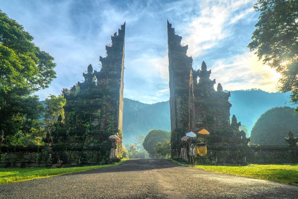 Traditional Balinese stone gate at Handara Gate, surrounded by lush greenery and misty mountains under a bright blue sky.