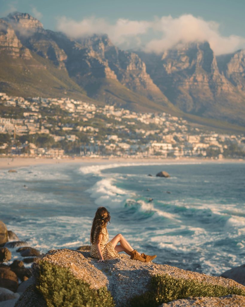 Woman sitting on rocks above Camps Bay with the Twelve Apostles, Cape Town.