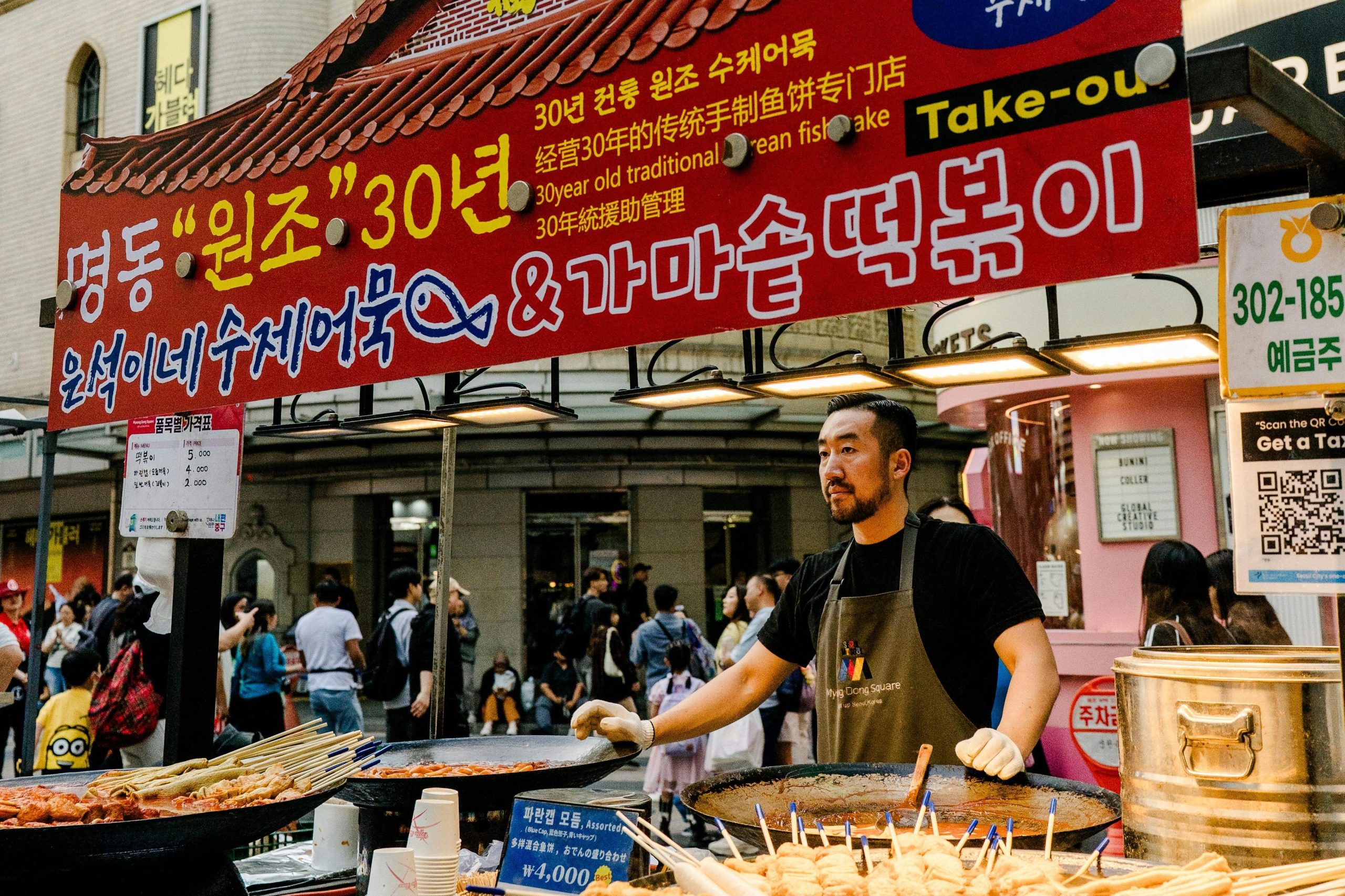 Street food vendor serving Korean fish cakes and tteokbokki at a busy market in Seoul.